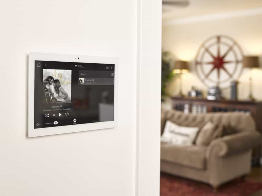 A smart device with multi-room audio capabilities is mounted on a wall in a living room.