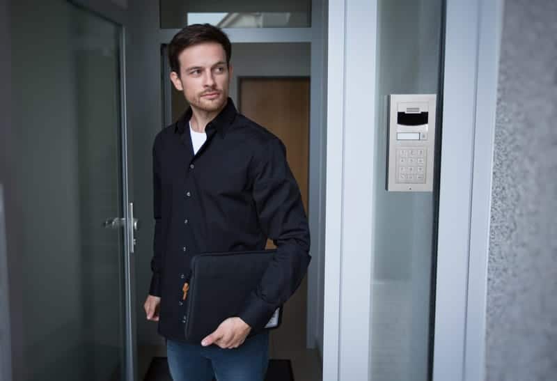 A man holding a briefcase while standing in front of a smart home security door.